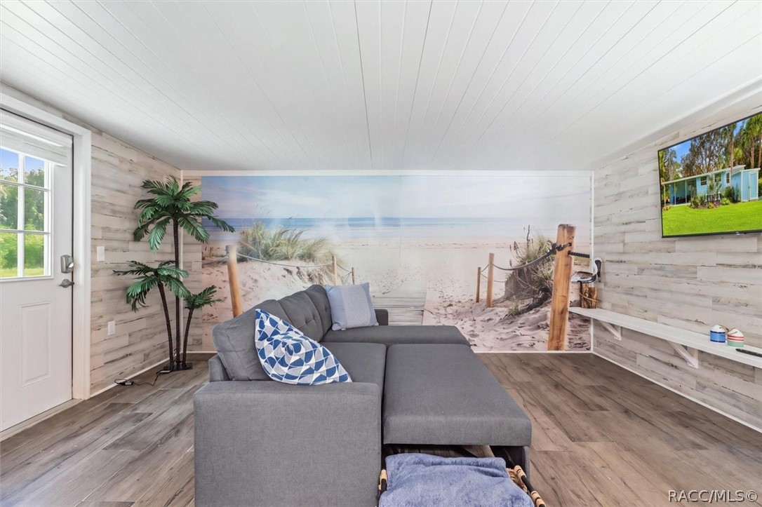 Furnished living room with a gray sectional, beach mural, and wood-look flooring.