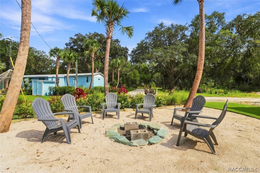 Outdoor seating area with gray Adirondack chairs around a fire pit, palms, and a blue home.