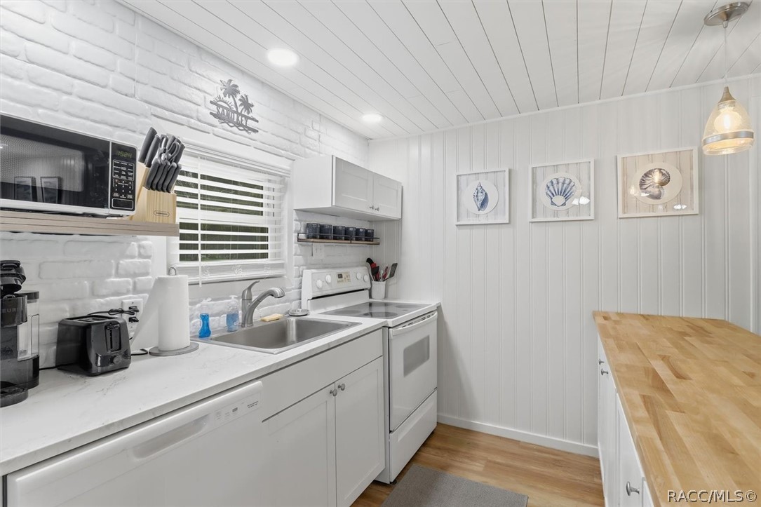 Bright white kitchen with a double sink, white appliances, and a butcher-block countertop.