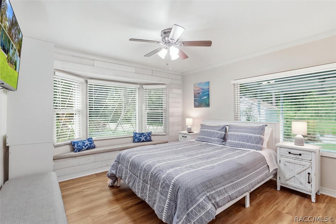 Bedroom with gray patterned bedding, a window-seat bench, and wide windows with blinds.