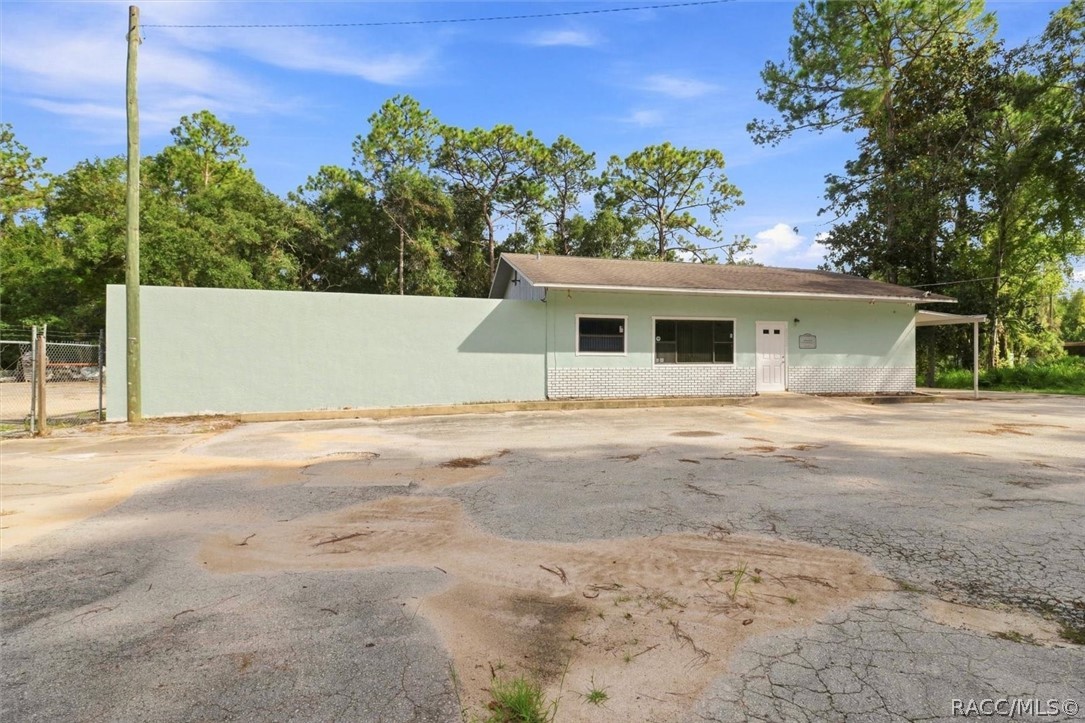 Single-story pale green building with a long wall beside a cracked paved lot.