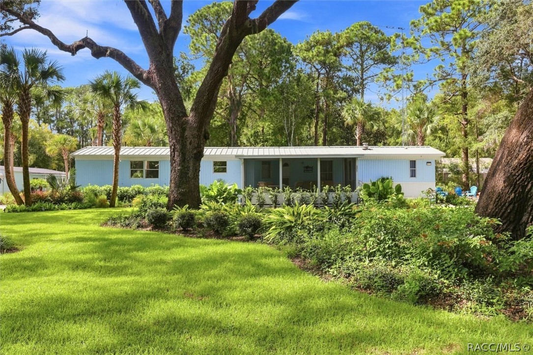 Single-story light-blue home with a covered porch, mature trees, and a landscaped lawn.