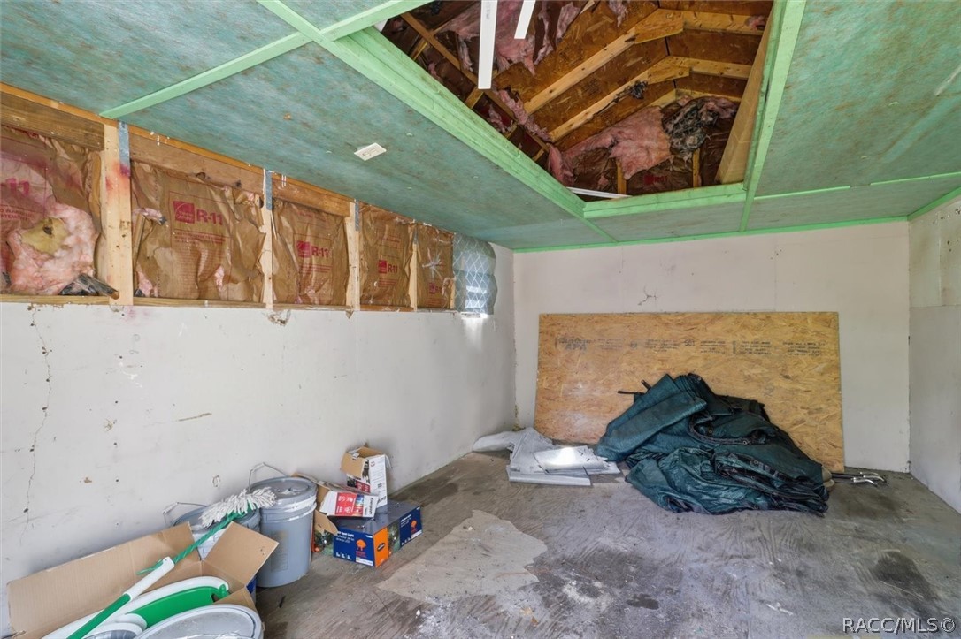 Unfinished garage with exposed insulation, missing ceiling sections, and construction debris.