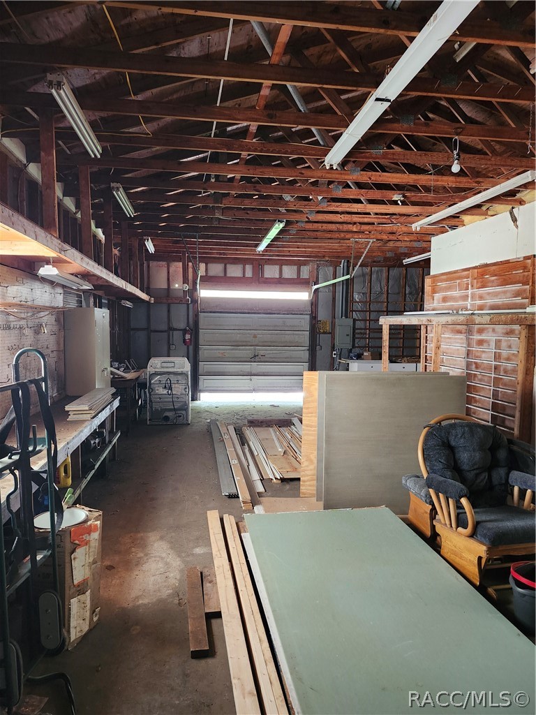 Workshop garage with exposed wooden rafters, workbenches, lumber, and a closed overhead door.