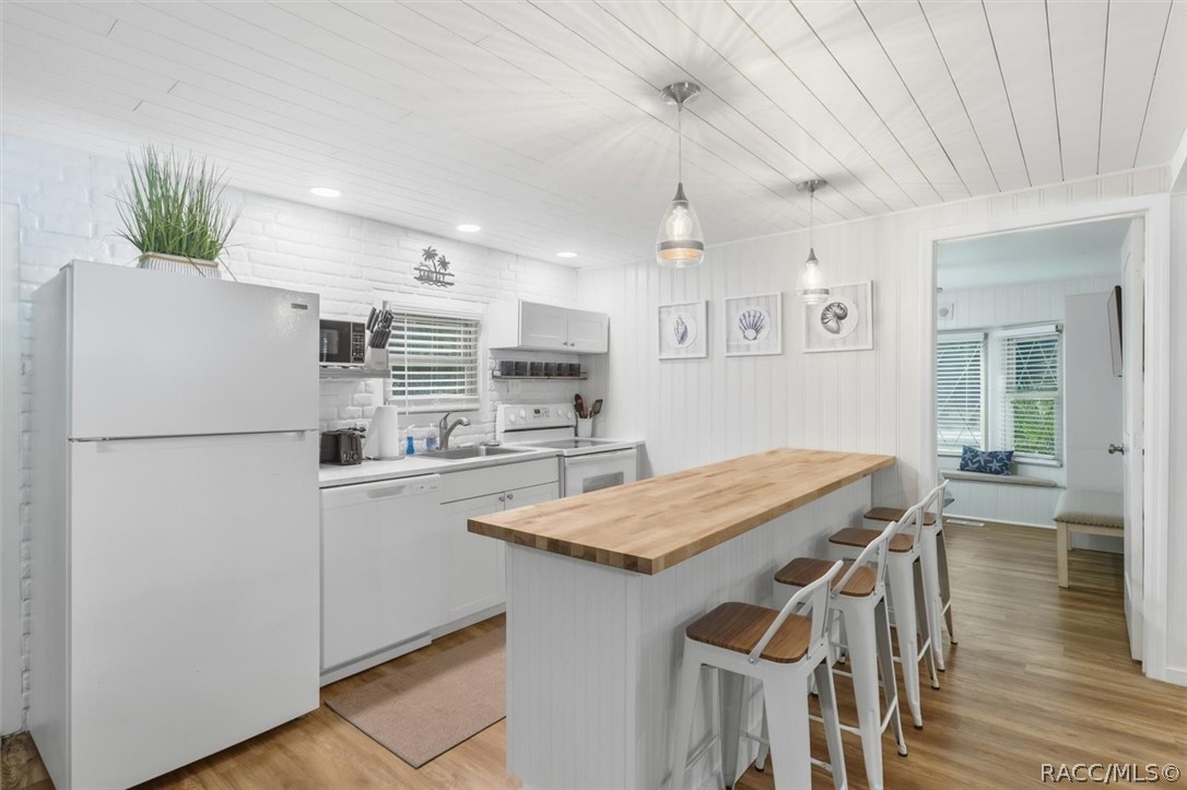 Bright white kitchen with a long butcher-block island, bar stools, and wood-look flooring.