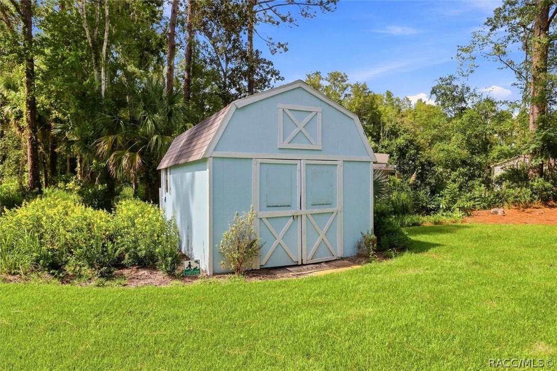 Light blue garden shed with white cross-braced doors on a lawn among trees.