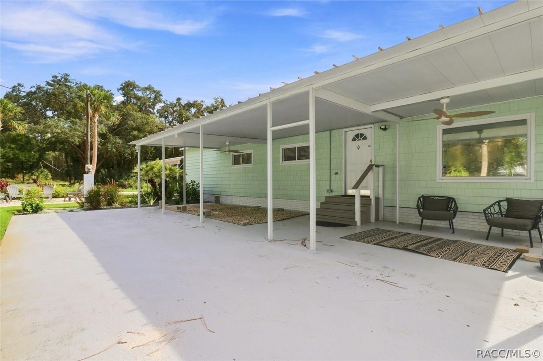 Mint-green home with a broad covered concrete patio, outdoor chairs, and rugs.