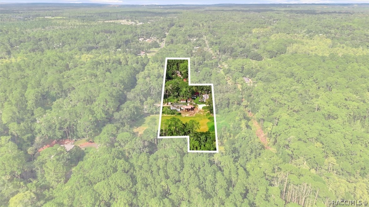 Aerial view of a wooded property outlined in white, with a central clearing and several buildings.