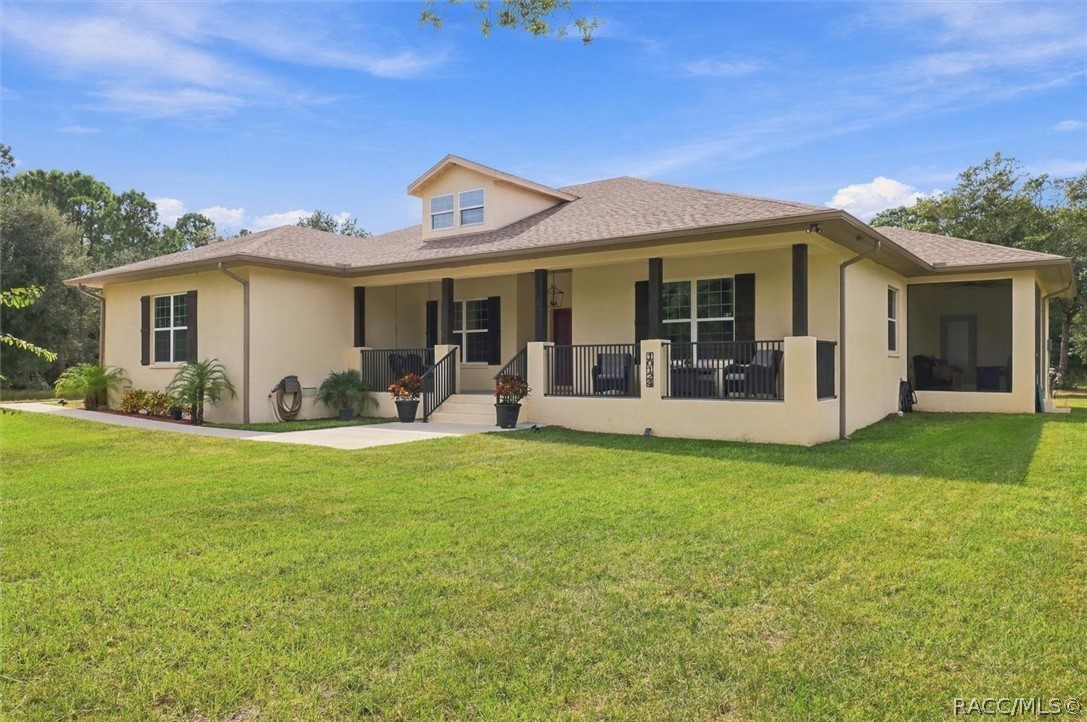 Beige home with a covered front porch, dark railings, dormer, and broad lawn.