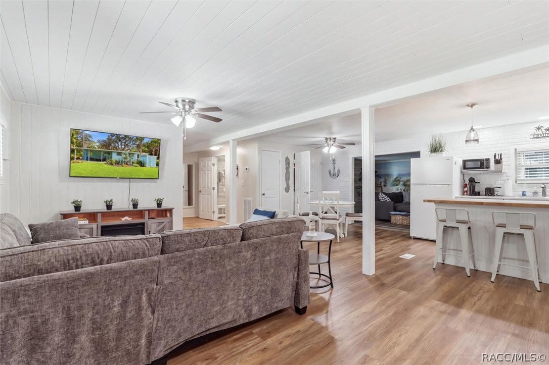 Open-plan living room and kitchen with gray sectional, white island, and wood-look floors.