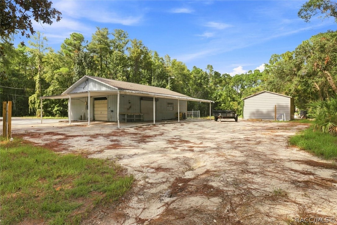 Outbuilding with a broad covered carport and separate shed on a wooded lot.