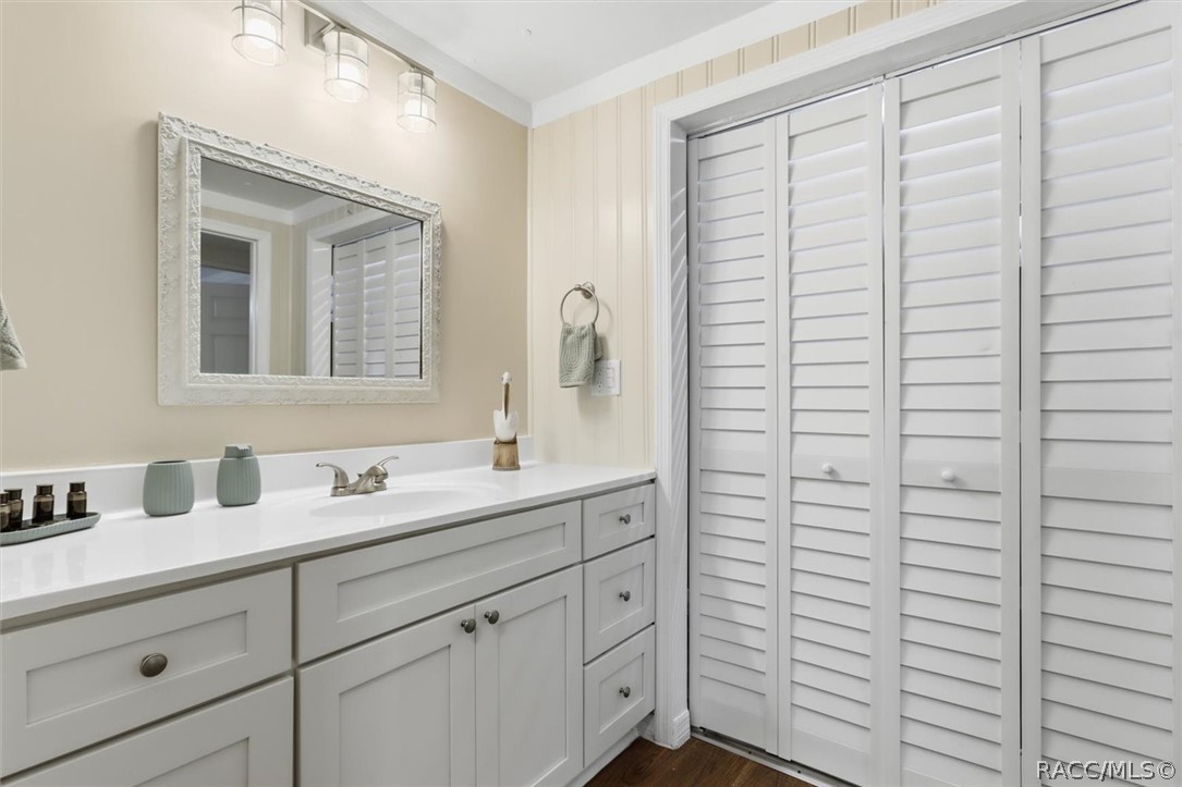 Bathroom with a white paneled vanity, framed mirror, and louvered closet doors.