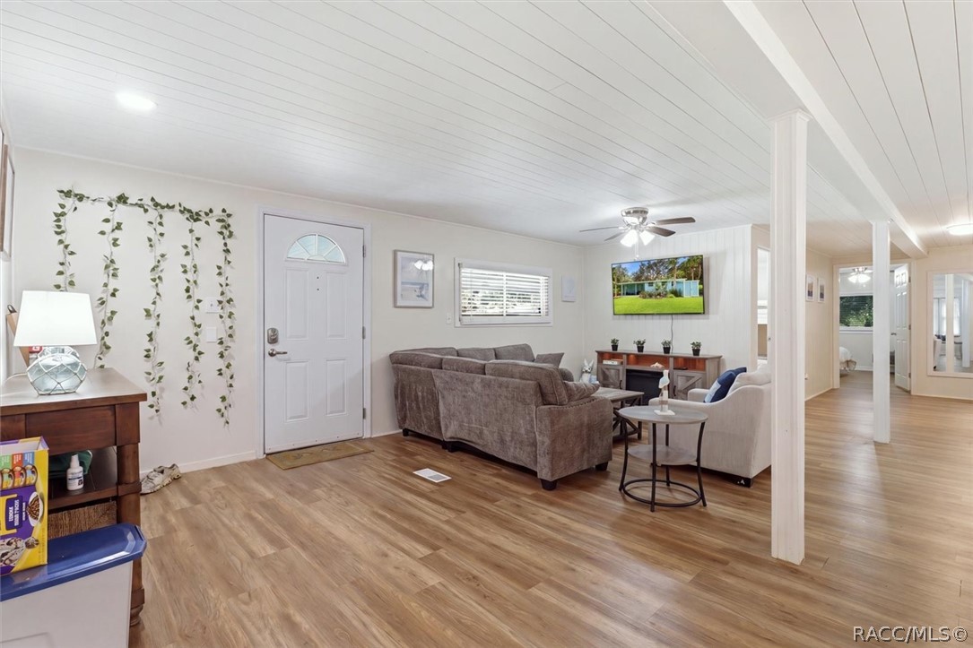 Living room with wood-look flooring, a white plank ceiling, and an open hallway.