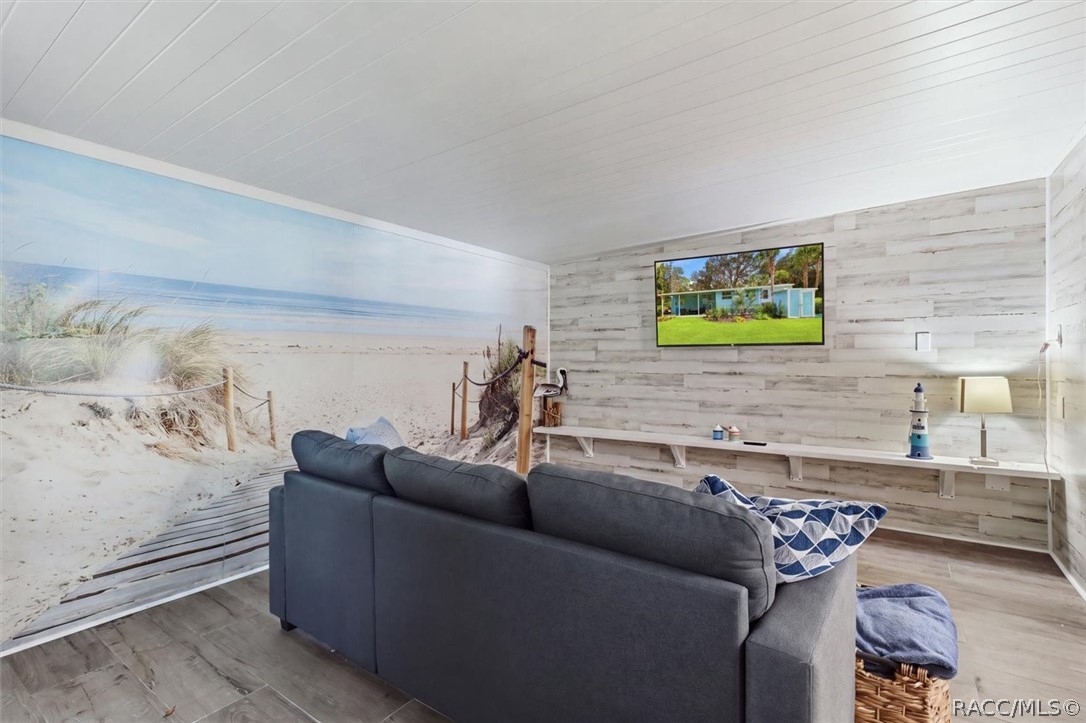 Furnished living room with a beach mural, dark gray sectional, and whitewashed wood walls.