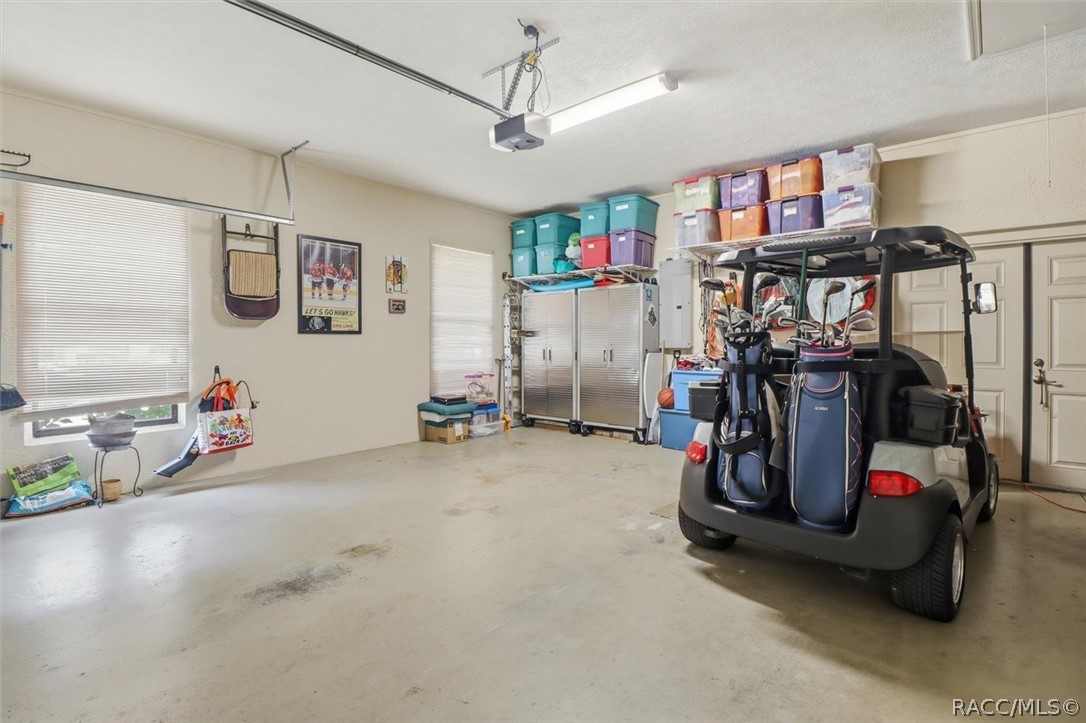 Garage with a golf cart carrying golf bags, storage cabinets, and colorful bins.