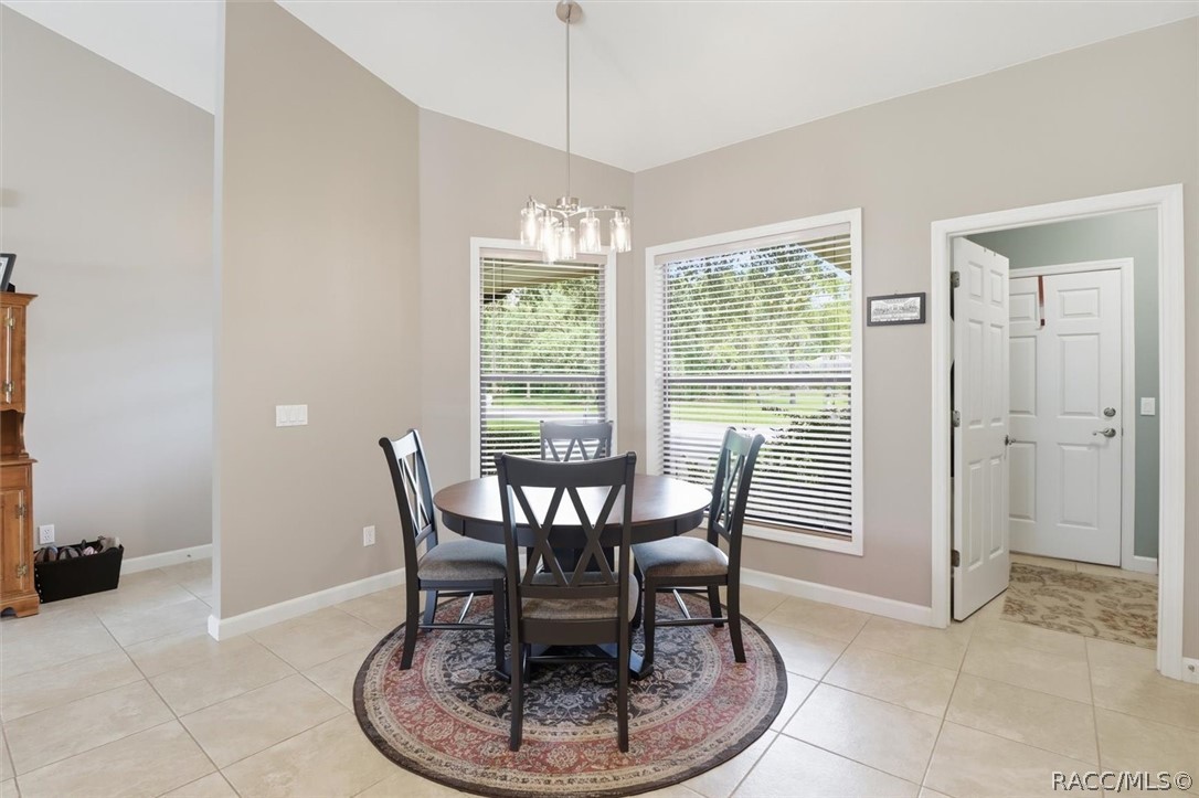 Dining area with a round table and chairs beneath a chandelier, beside two large windows.