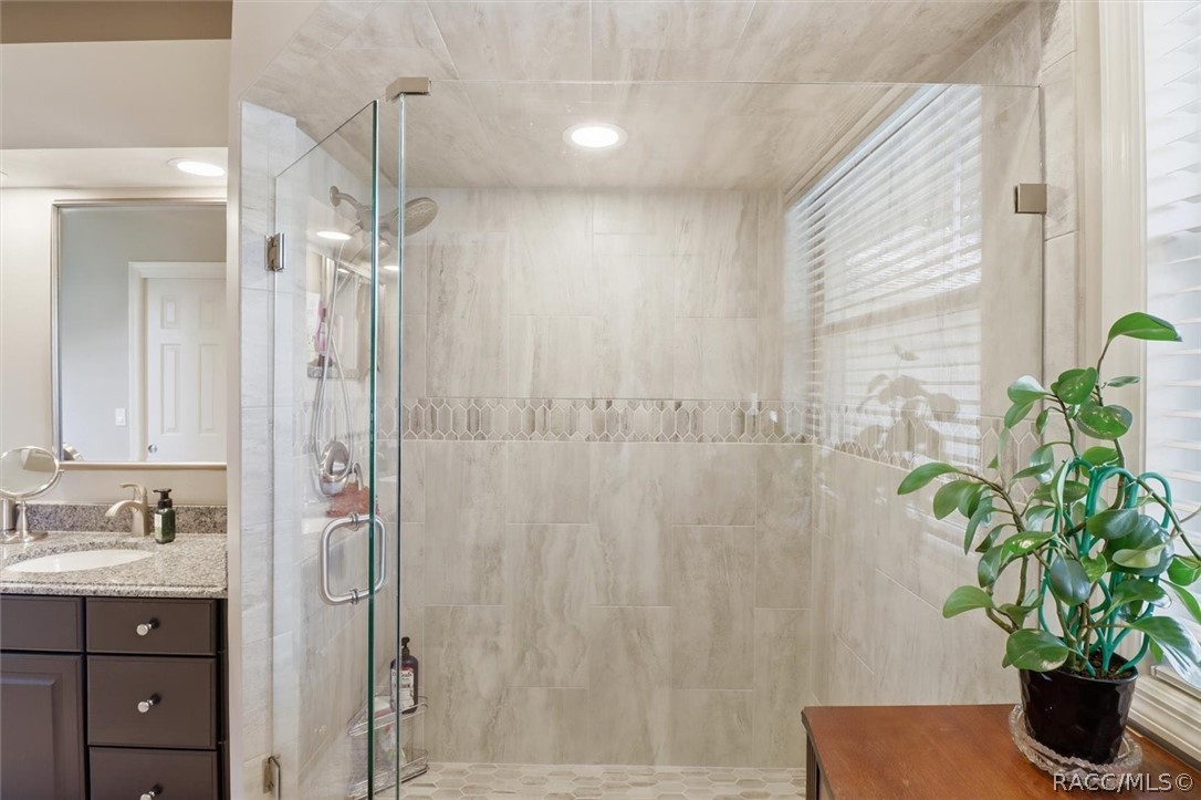 Bathroom with a glass-enclosed tiled shower, granite vanity, and window blinds.