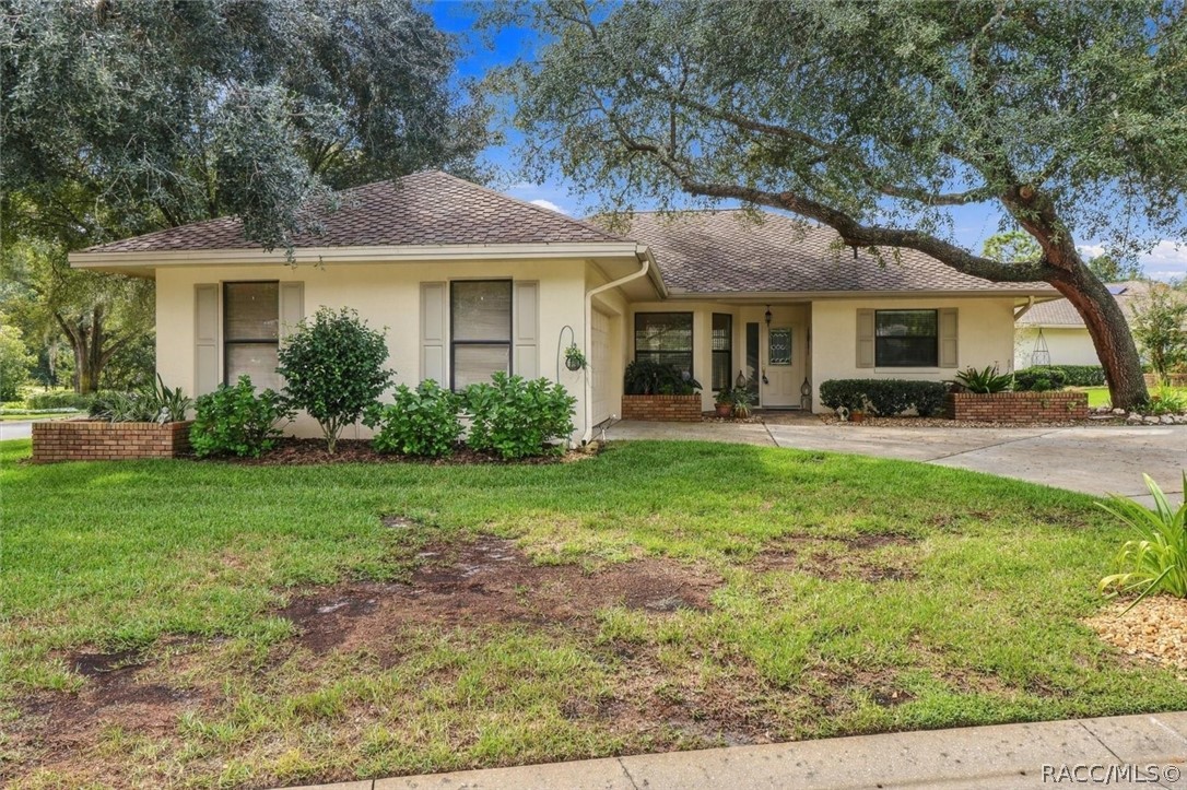 Single-story cream house with a tiled roof, brick planters, and a large oak tree.
