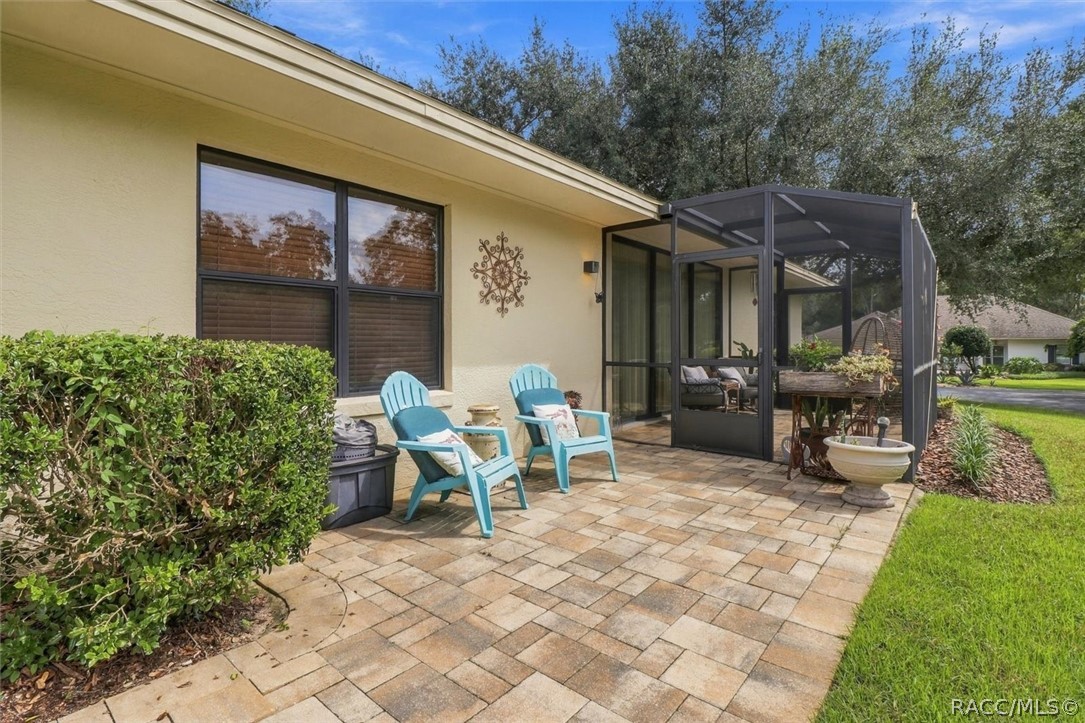 Paved backyard patio with turquoise chairs beside a screened-in sunroom and green lawn.