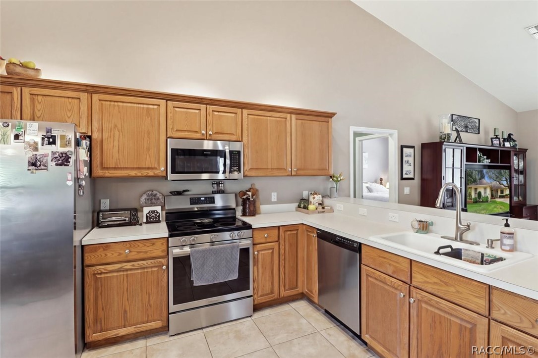 Kitchen with honey-oak cabinets, stainless steel appliances, and a long white countertop with an undermount sink.