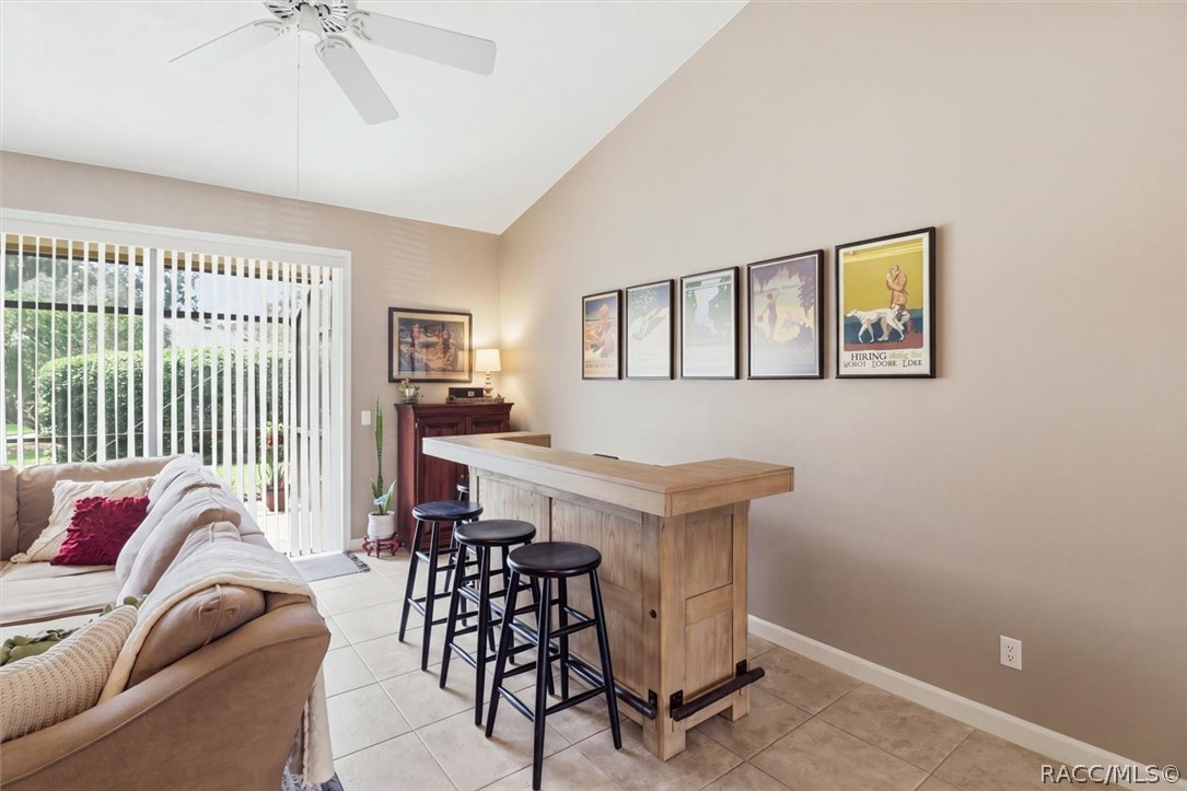 Living room with a wooden bar counter and stools beside a sofa and sliding glass doors.