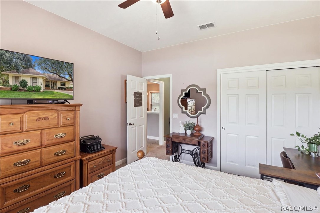 Furnished bedroom with a white quilted bed, wooden dressers, and a ceiling fan.