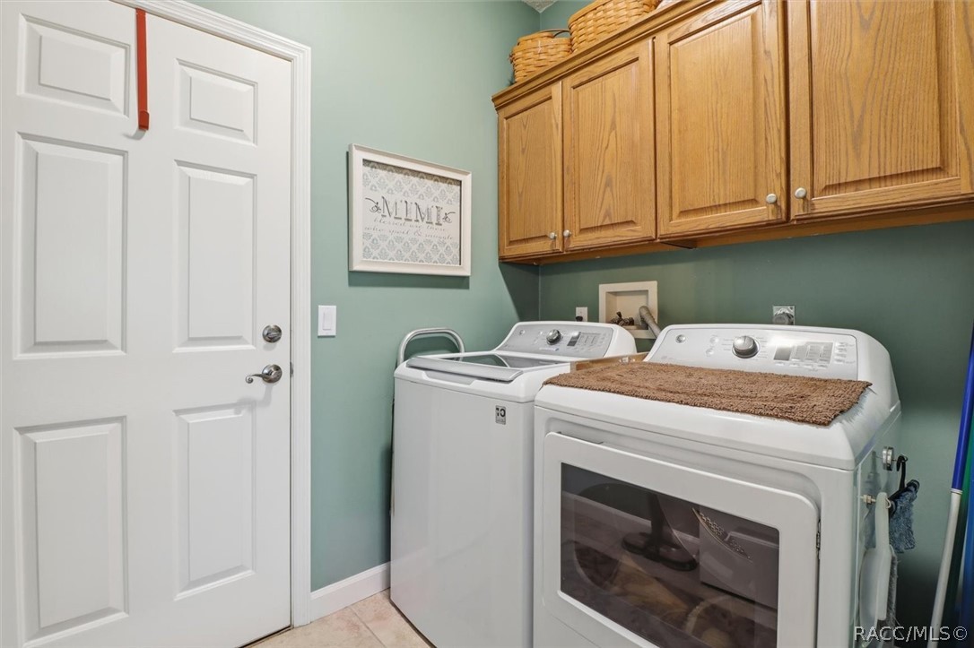 Laundry room with white washer and dryer beneath wooden cabinets.