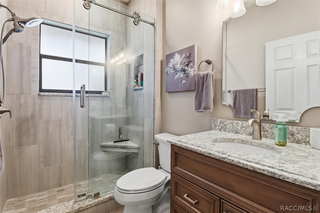 Bathroom with a glass-enclosed tiled shower, granite vanity, and wooden cabinetry.