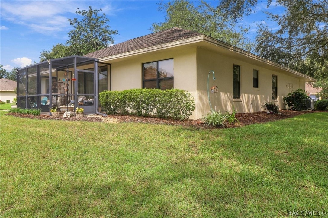 Single-story beige home with a screened lanai, trimmed shrubs, and a broad green lawn.