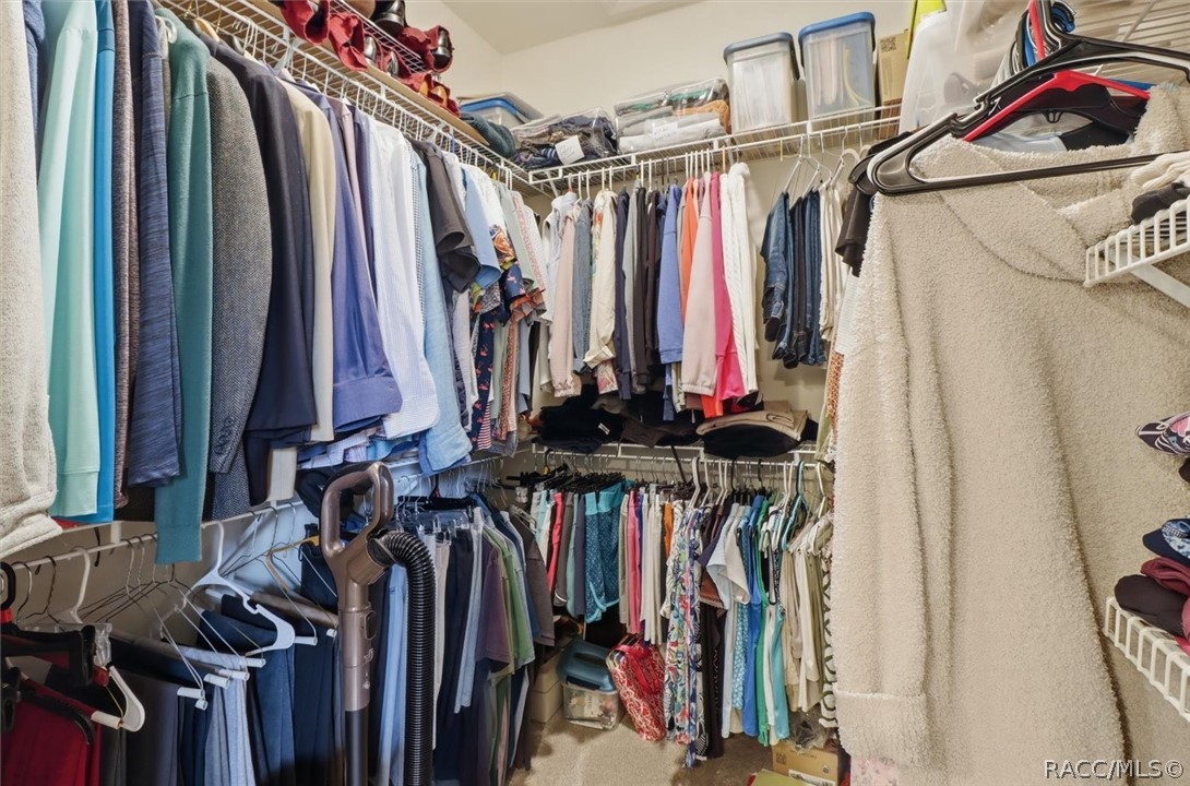 Walk-in closet with clothing on multiple racks and storage containers on upper shelves.