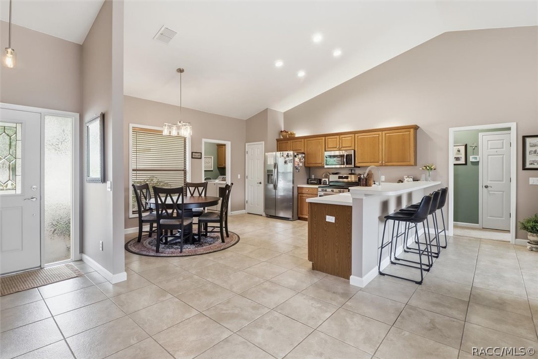 Open kitchen and dining area with wood cabinets, tiled floors, and a white breakfast bar.