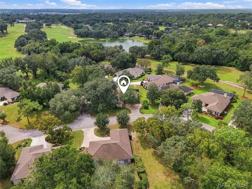 Aerial view of a tree-lined neighborhood beside a golf course and lake, with the listed home marked.
