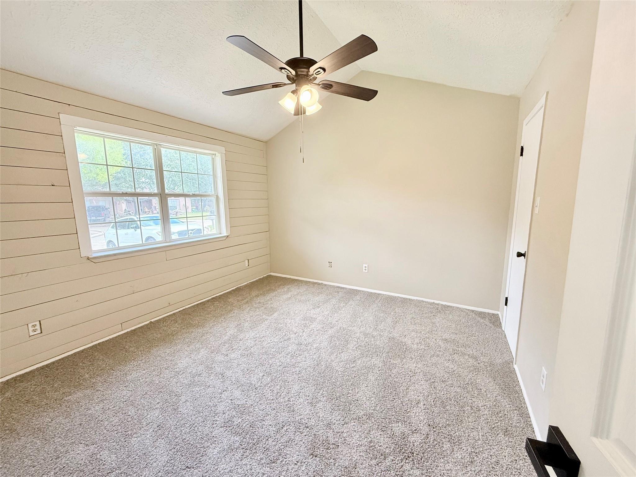 Empty bedroom with carpet, a plank accent wall, large window, and ceiling fan.