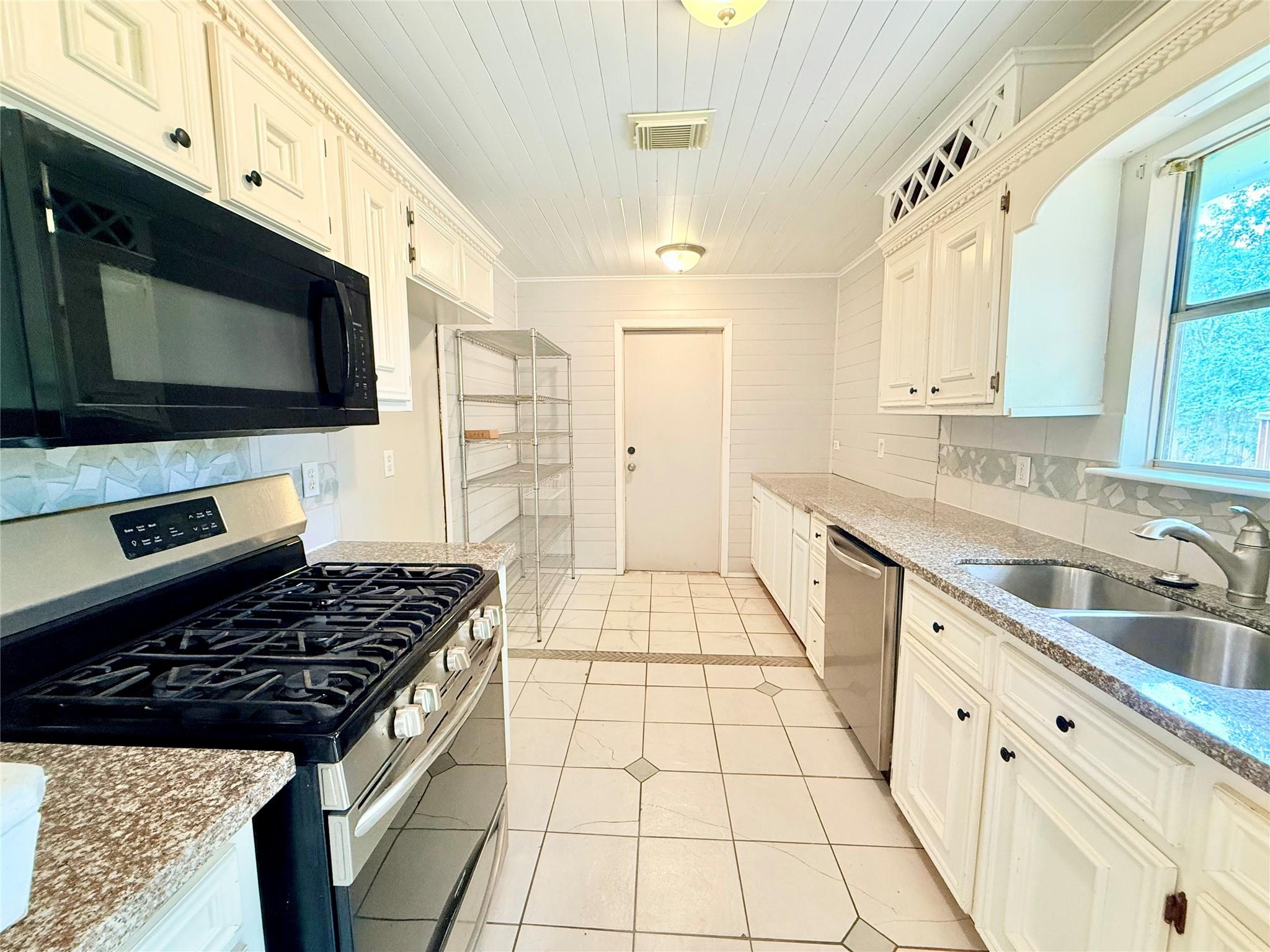 Galley kitchen with white cabinets, black gas range, stainless dishwasher, and double-basin sink.