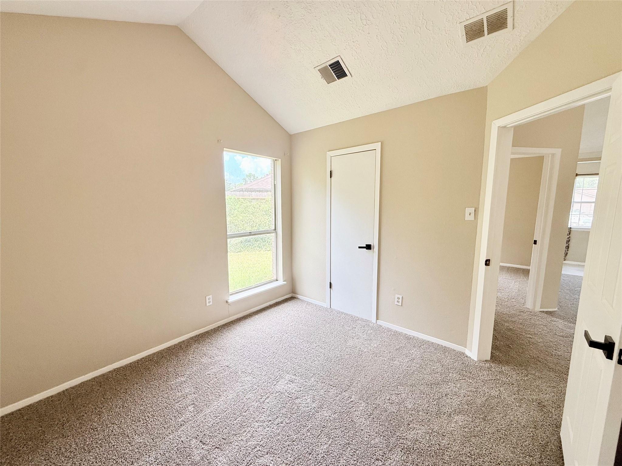 Empty bedroom with a vaulted ceiling, large window, and wall-to-wall carpet.