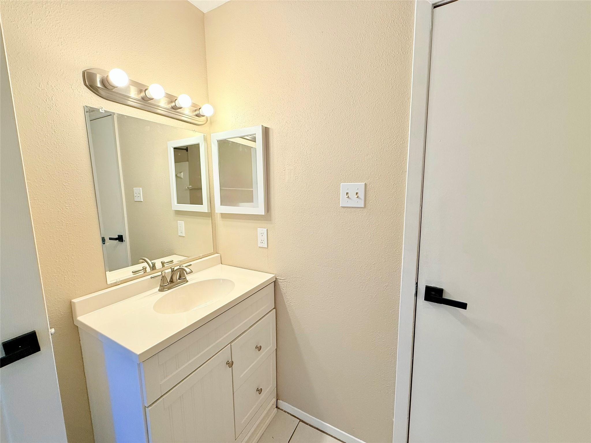 Bathroom vanity with a white sink, large mirror, and four-bulb light fixture.