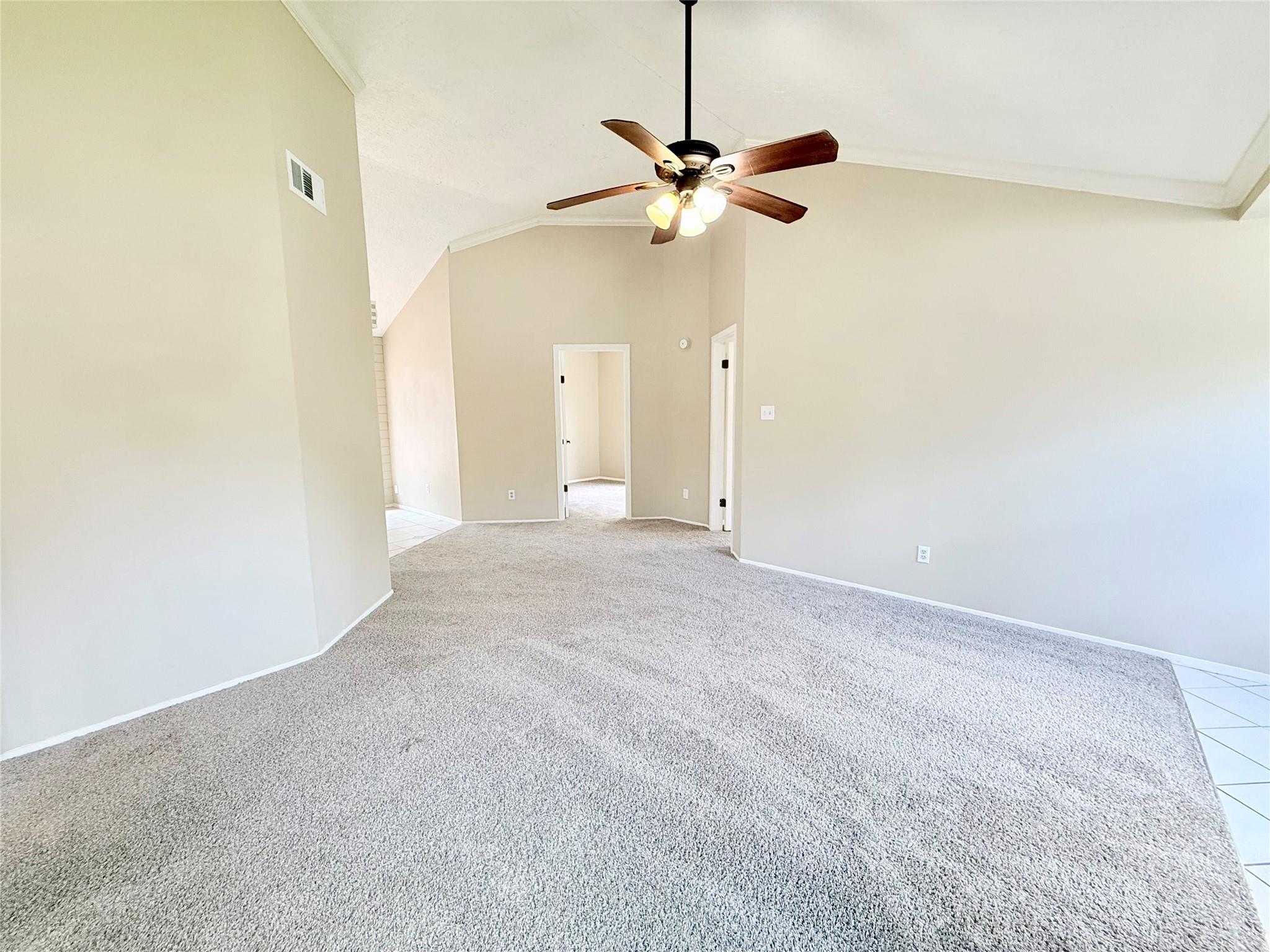 Empty carpeted living room with a vaulted ceiling and ceiling fan.