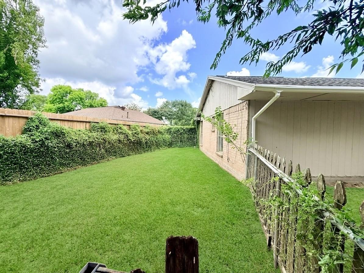Fenced backyard with a broad green lawn, tall hedges, and the side of the house.