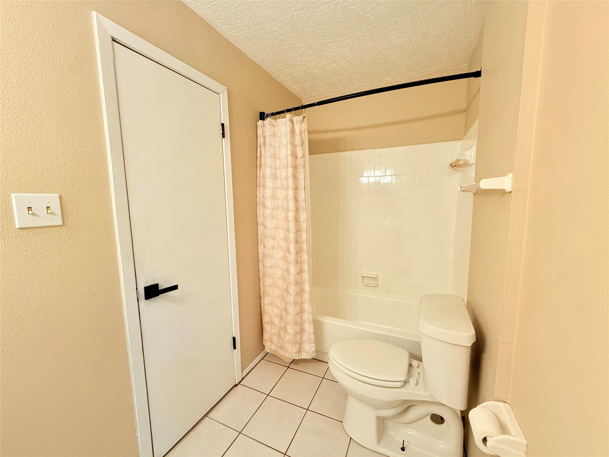 Bathroom with a tiled tub and shower, patterned curtain, and toilet.