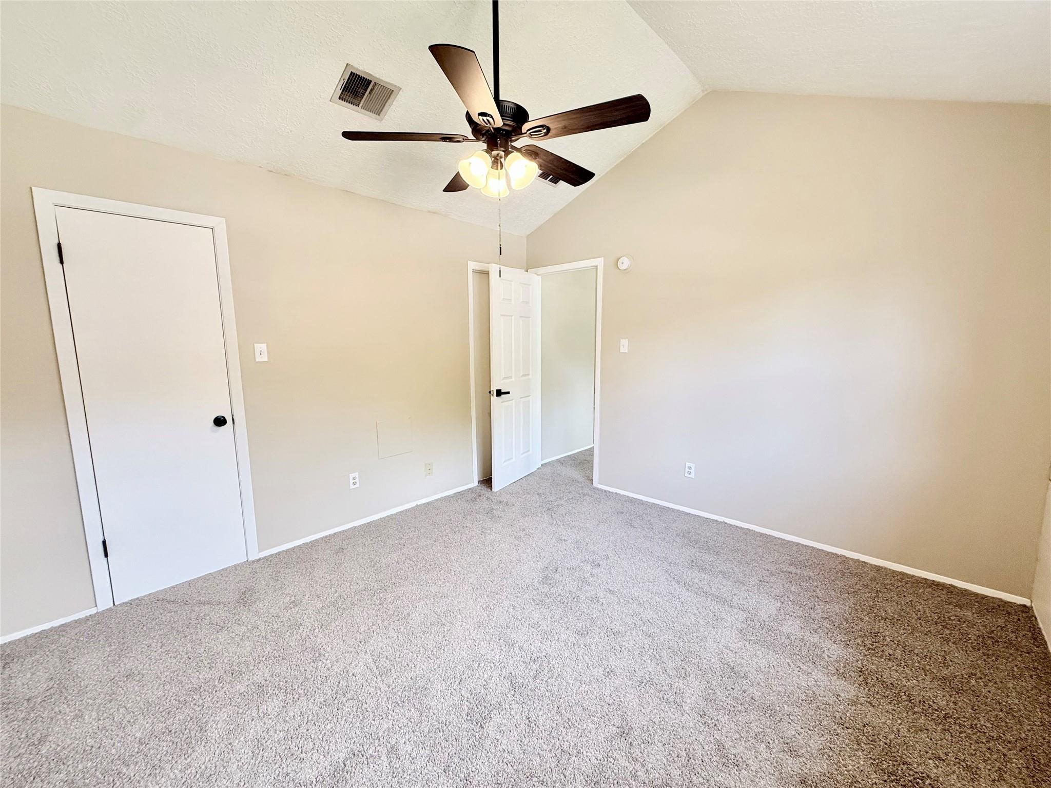 Empty bedroom with gray carpet and a ceiling fan with lit bulbs.