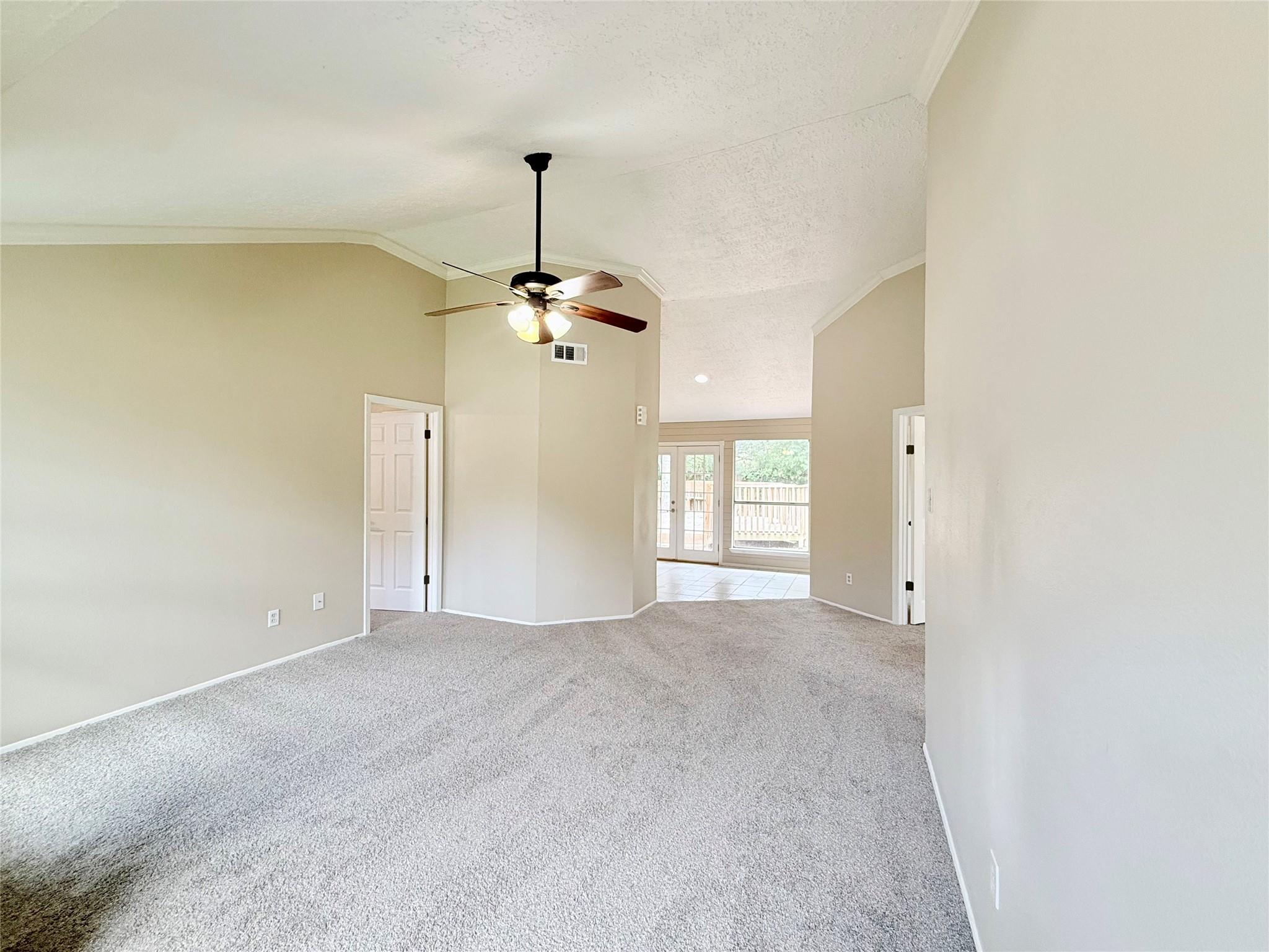 Empty living room with vaulted ceiling, gray carpet, ceiling fan, and glass doors to the backyard.