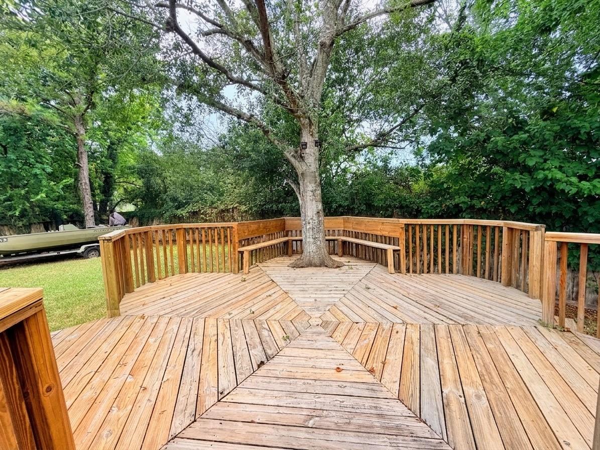 Wooden backyard deck with built-in benches around a mature tree and a leafy yard beyond.