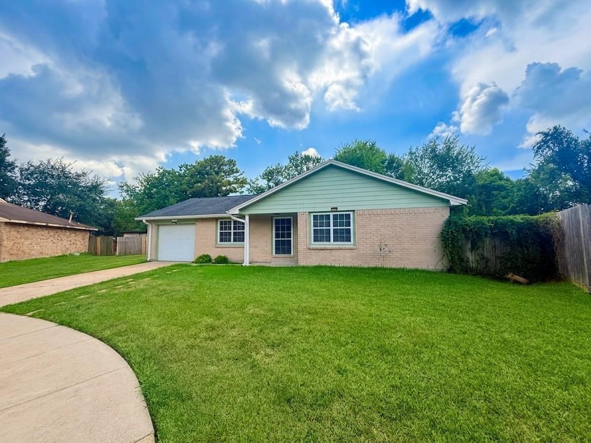 Single-story brick house with an attached garage, broad green lawn, and curved concrete walkway.