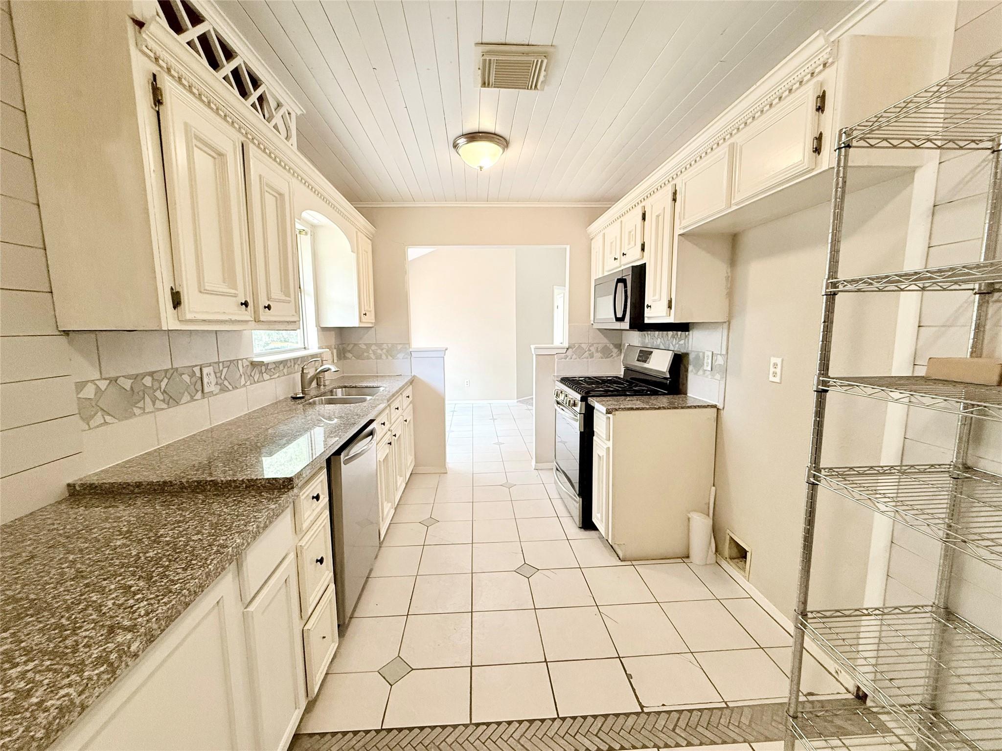 Kitchen with cream cabinets, granite counters, stainless-steel dishwasher, and gas range.