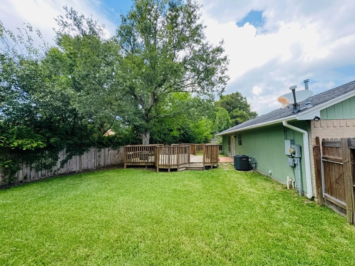 Backyard with broad lawn, raised wooden deck, mature trees, and a wooden privacy fence.