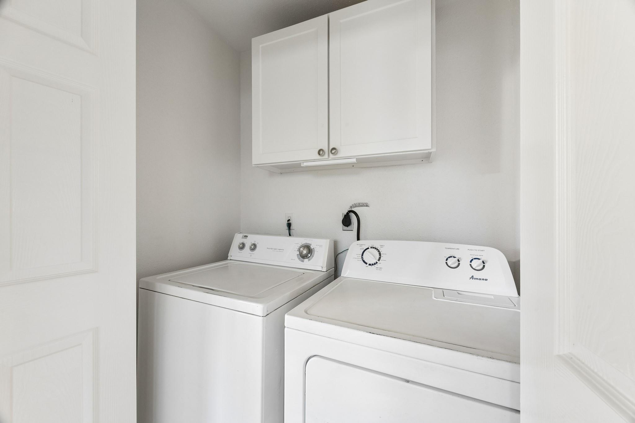 Laundry room with a washer and dryer beneath wall cabinets.