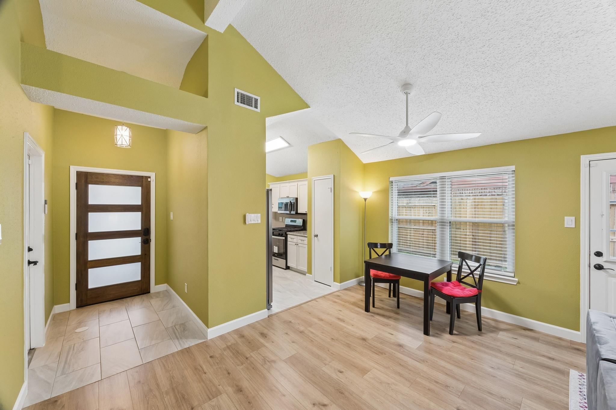 Open entry and dining area with vaulted ceiling, yellow-green walls, and a small table by the window.