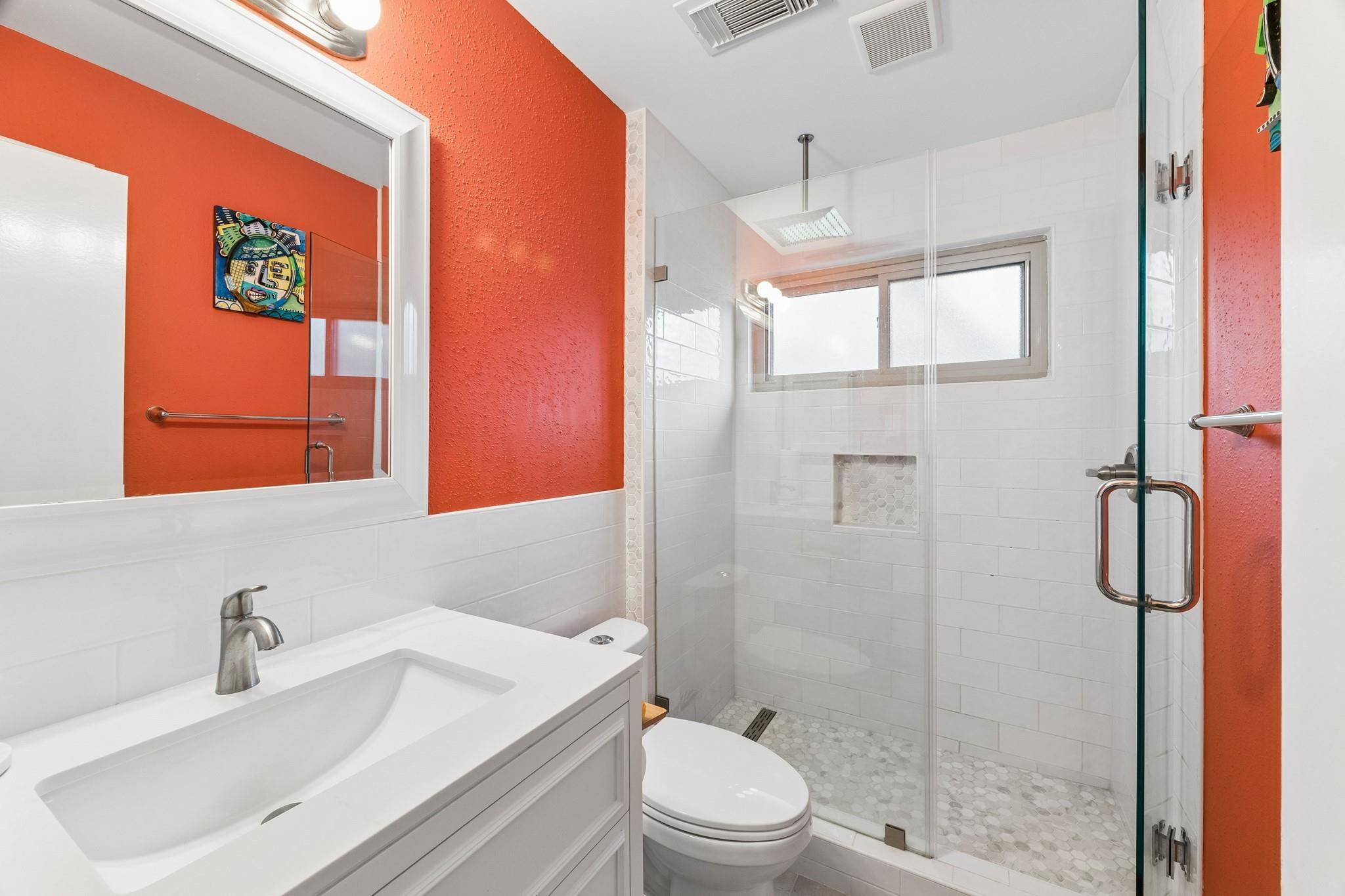 Bathroom with glass walk-in shower, white vanity, and vivid orange walls.