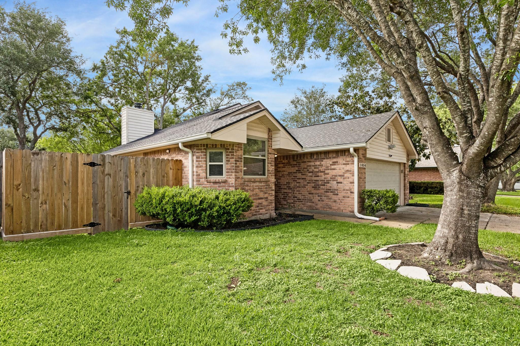Brick home with an attached garage, wooden fence, and large shade tree in the front yard.