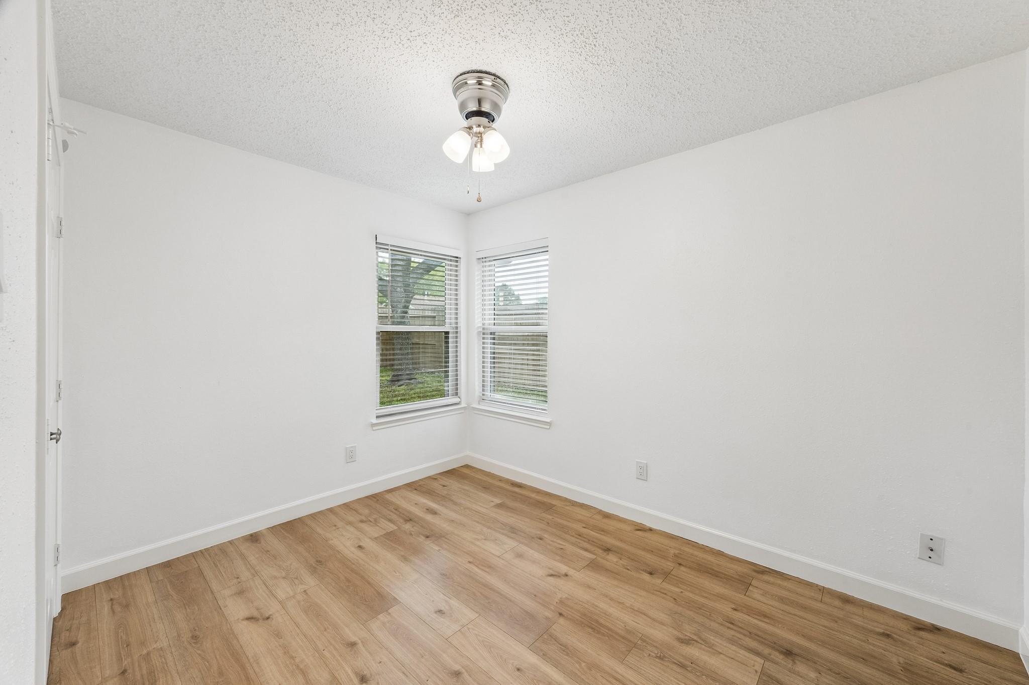 Empty room with wood-look flooring, two corner windows with blinds, and a ceiling fan.